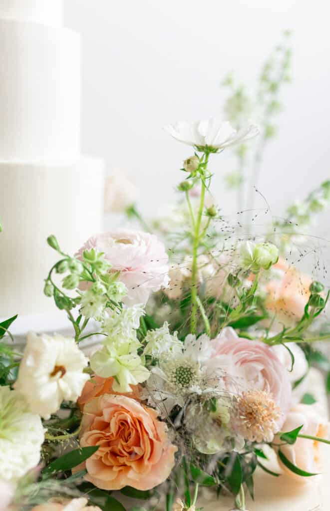 3 tiered white wedding cake surrounded by flowers